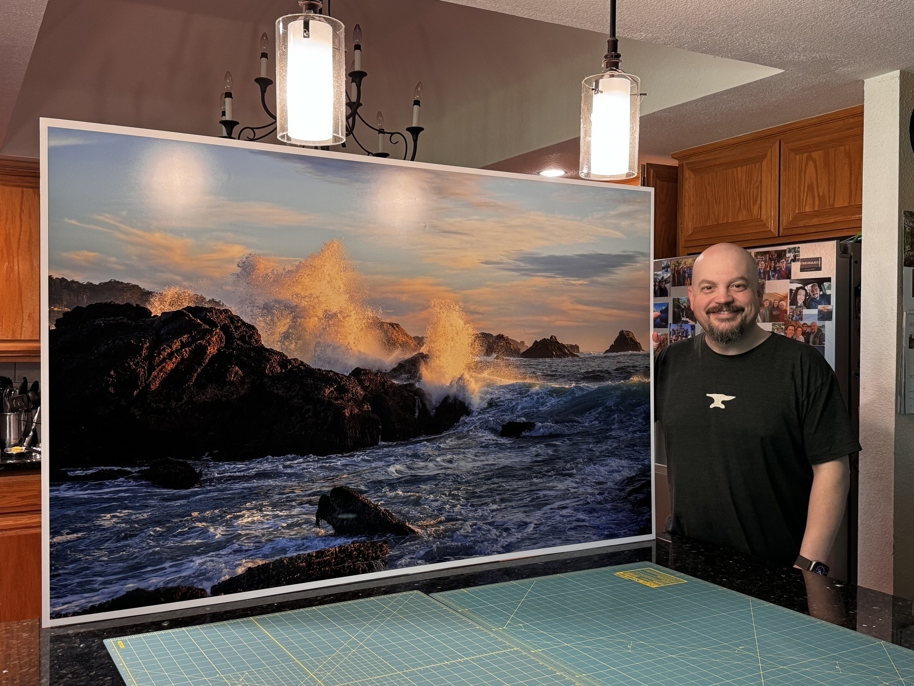 Kirk standing with a very large photo print of a wave crashing onto rocks.
